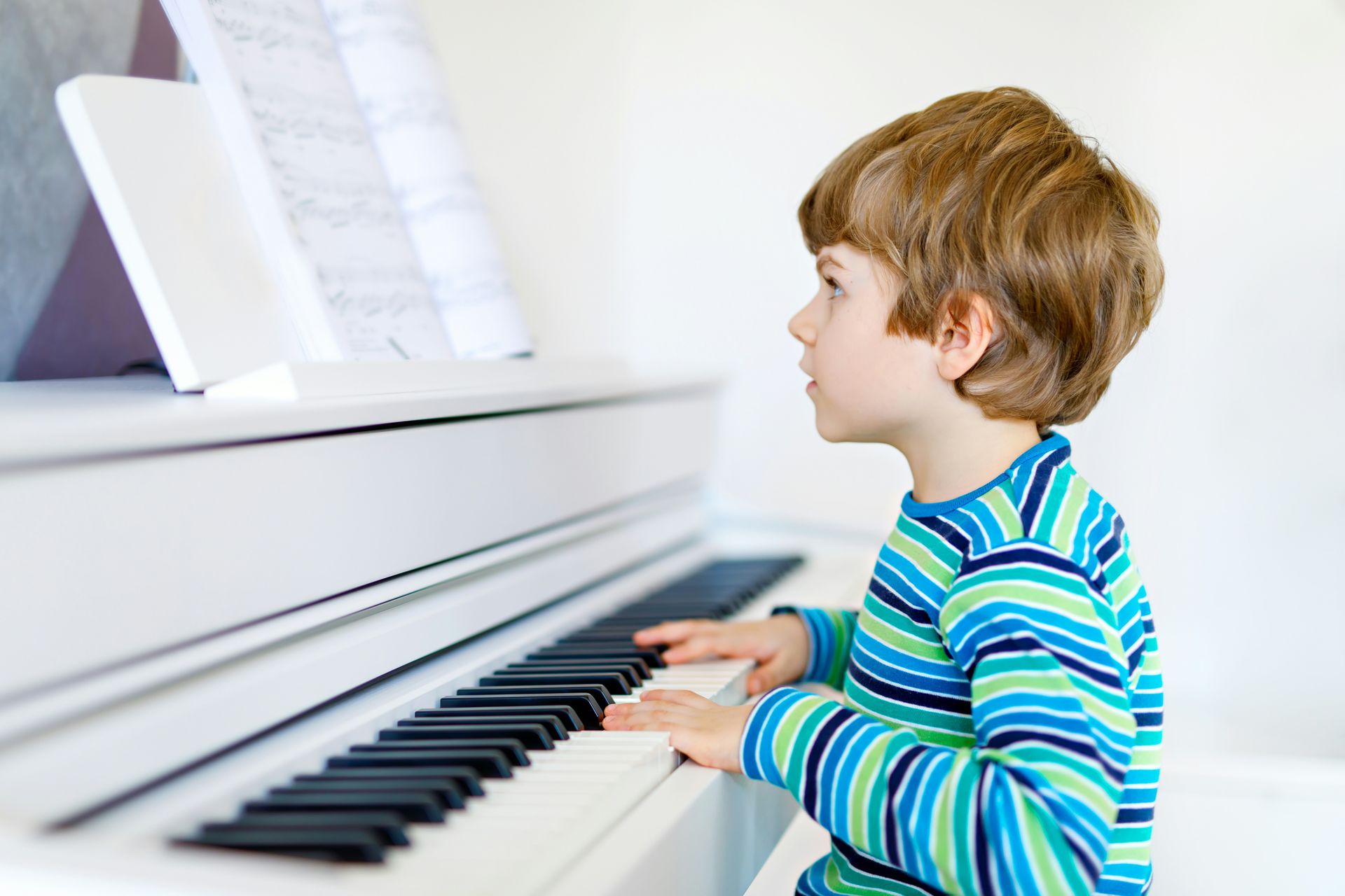 A young boy playing a white piano, with sheet music on the stand.