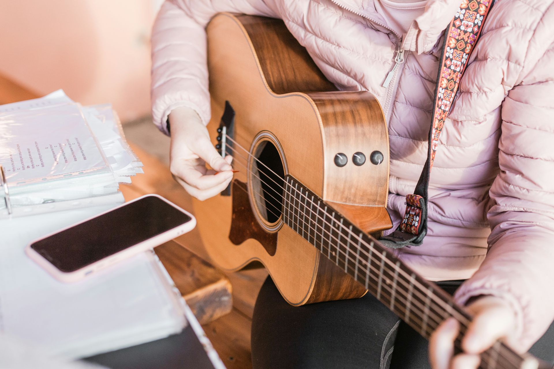 A person playing an acoustic guitar beside a smartphone with its screen dark.