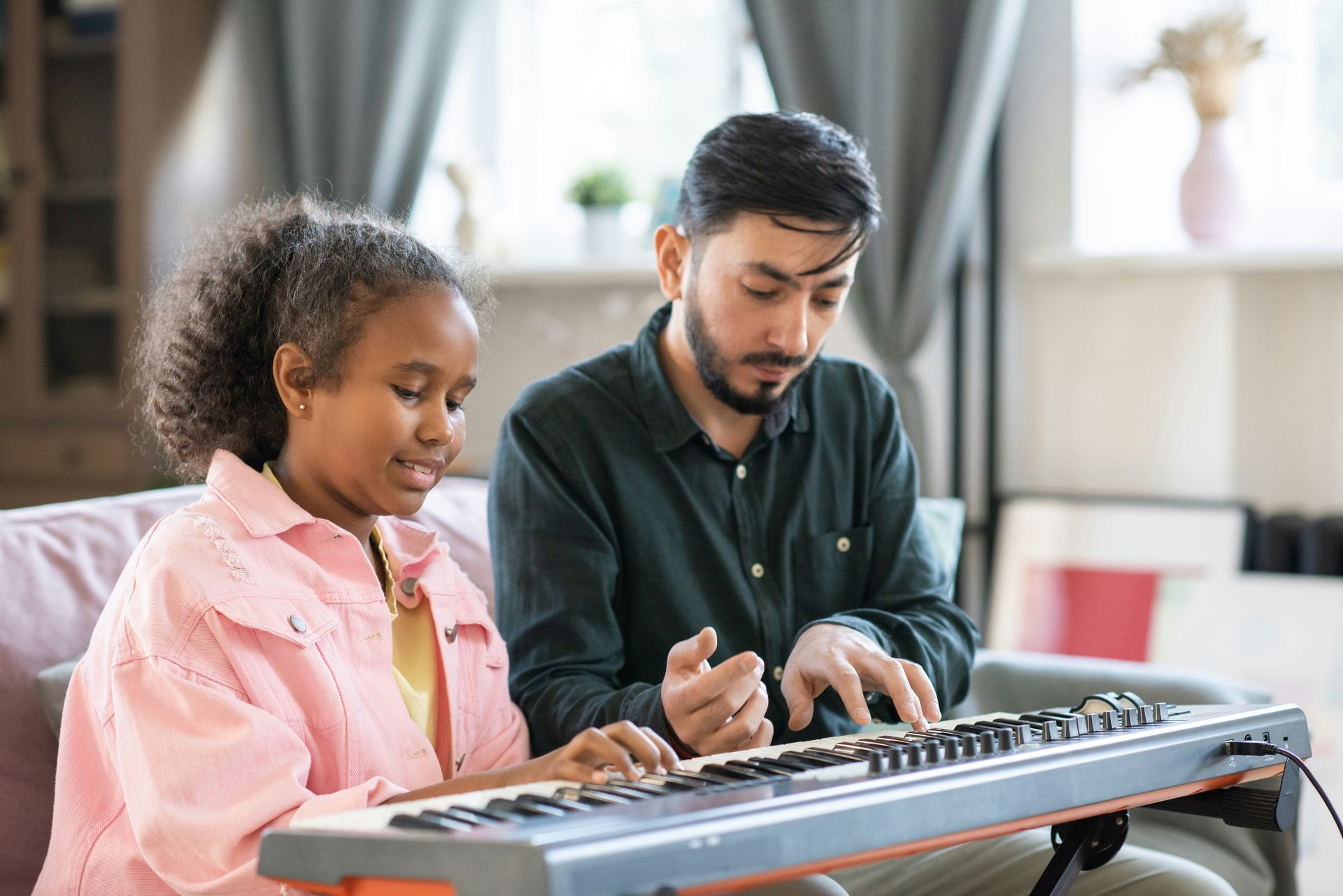 A music teacher gives guidance to a student playing an electronic keyboard.